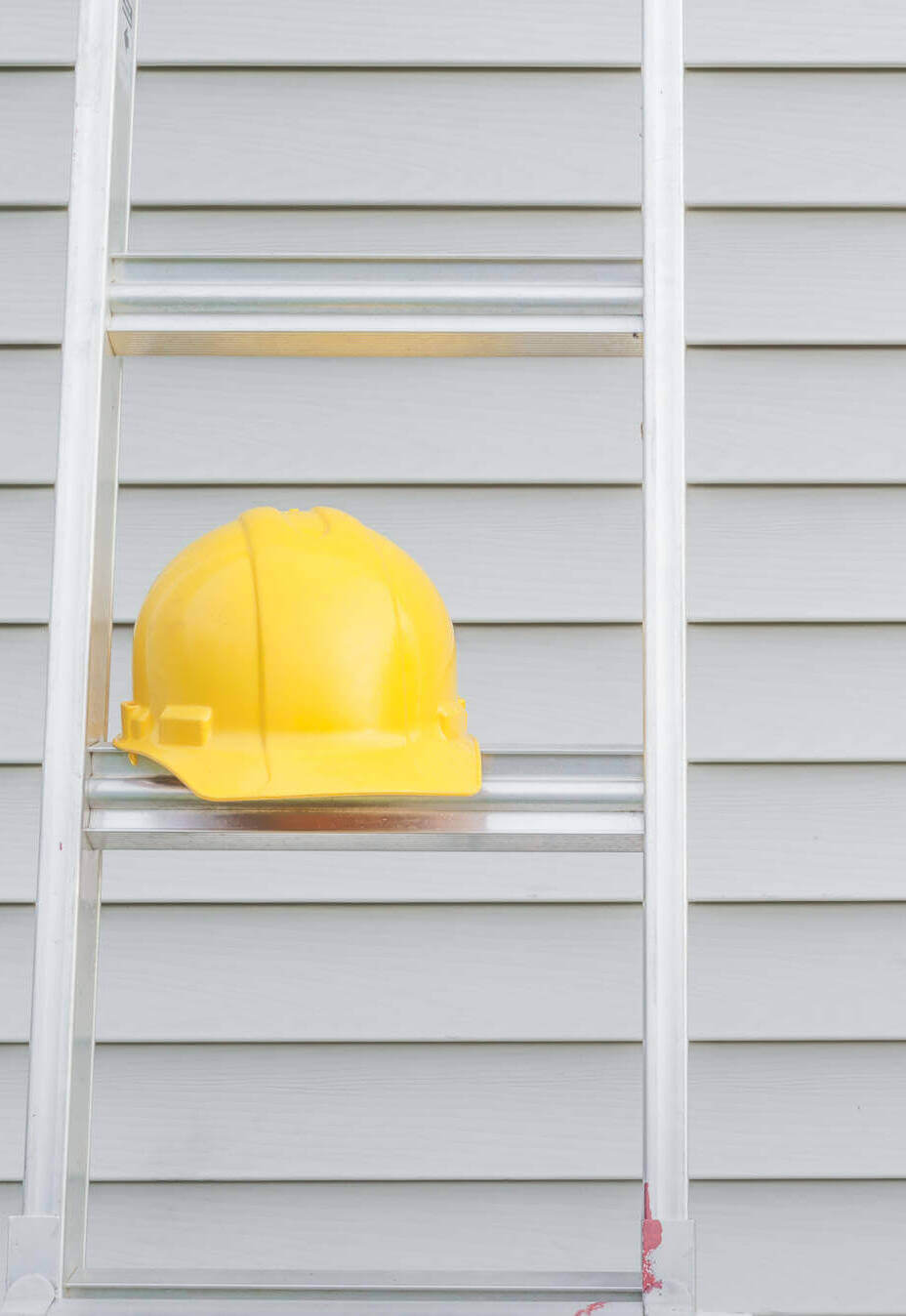 Yellow Hardhat On Ladder With House Siding In Background.